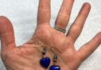 a hand holding a pair of blue heart earrings
