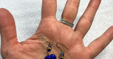 a hand holding a pair of blue heart earrings