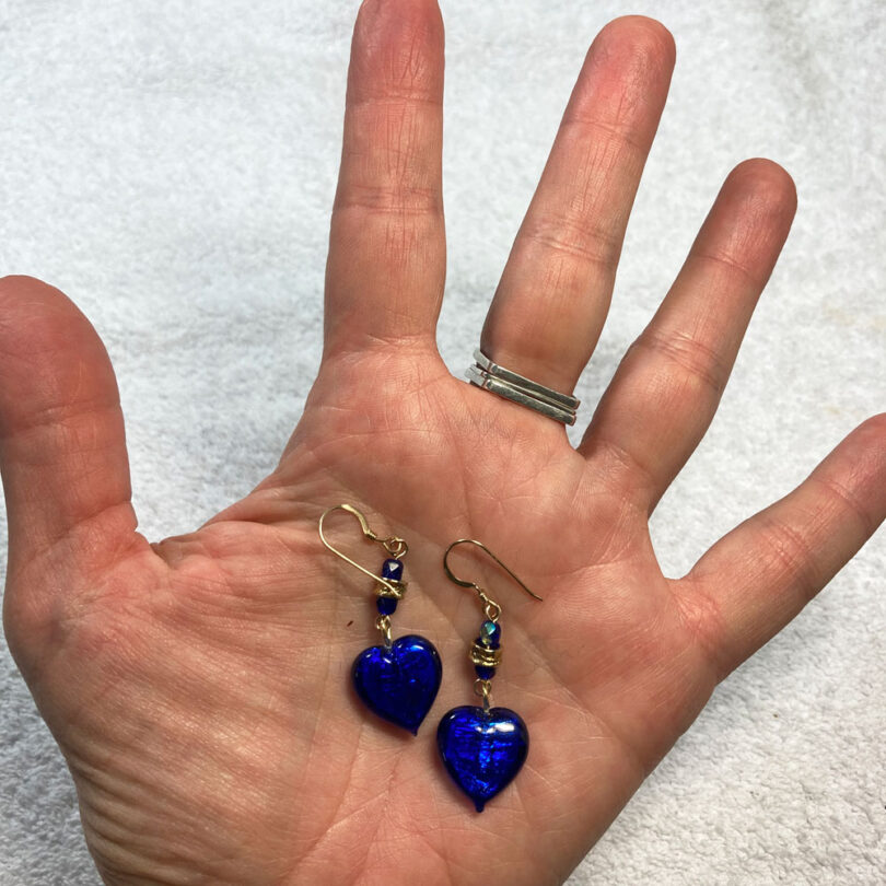 a hand holding a pair of blue heart earrings