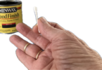a person holding a cotton swab with liquid stain in a can