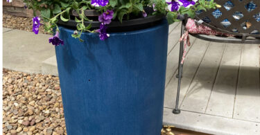a blue rain barrel with purple flowers and a copper watering can